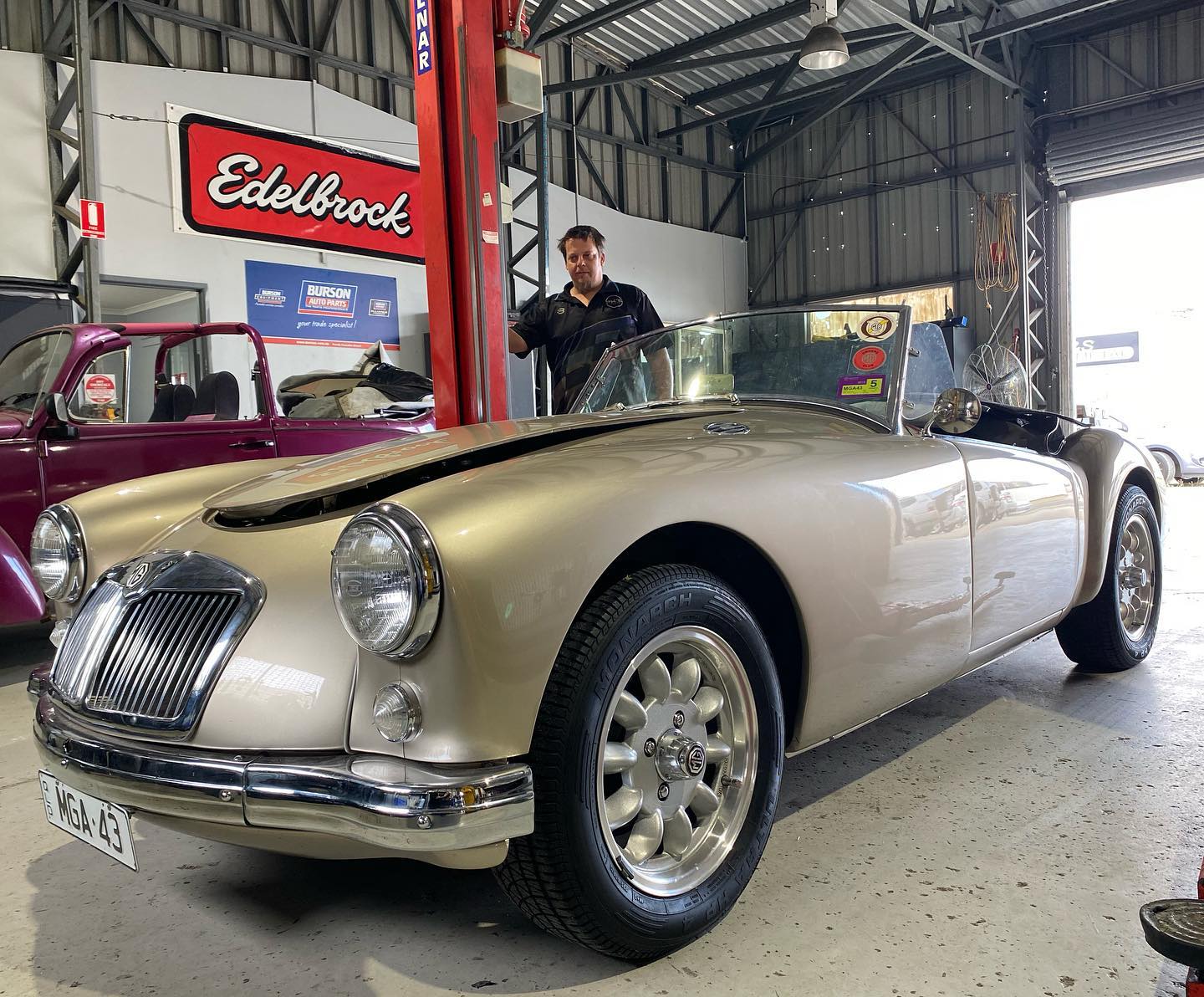 Gold MGA roadster in the workshop with a Bowser mechanic standing behind it
